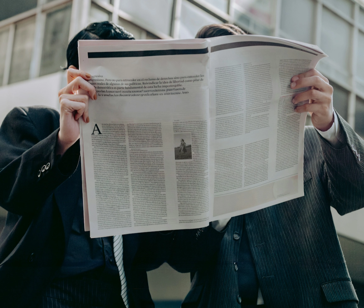 Two business men in suits holding up a newspaper and reading it.