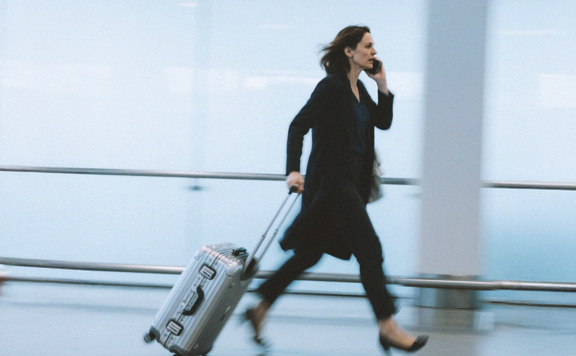A man sitting on a chair with one leg crossed over the other. The person is wearing suit pants and chunky brown shoes.The background features wooden cabinets and a wooden floor with a herringbone pattern.